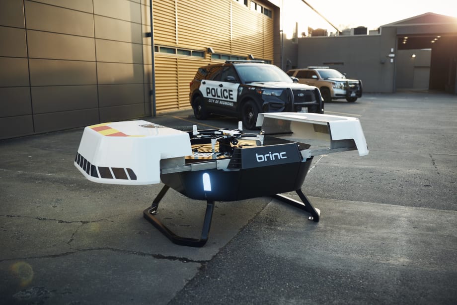 A Responder drone sits atop a Responder Station charging nest with two law enforcement vehicles in the background.