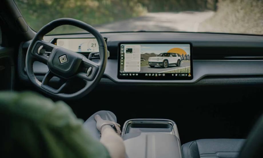 Interior view of a Rivian vehicle showing steering wheel and digital display screen with vehicle interface, representing autonomous technology development.