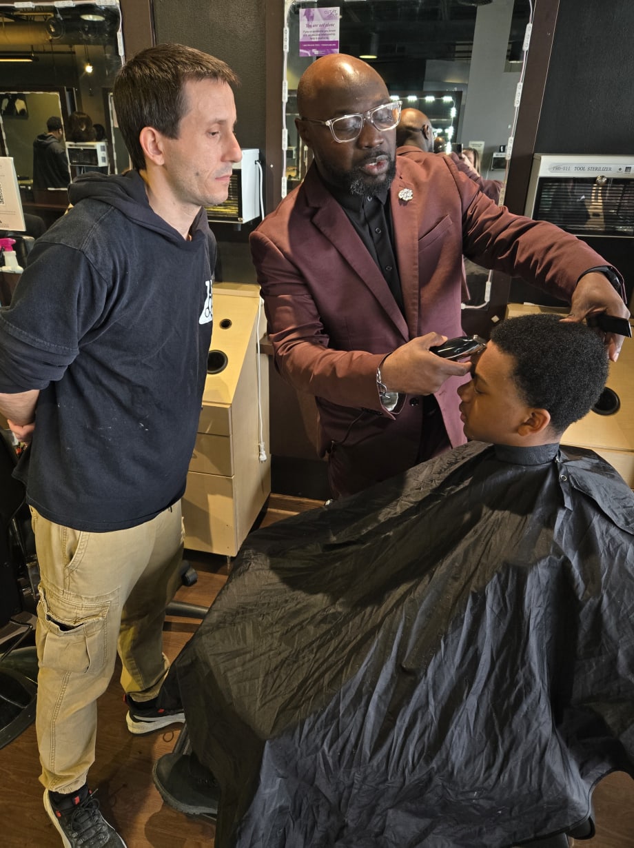 A barbering instructor works on a client while a student observes.