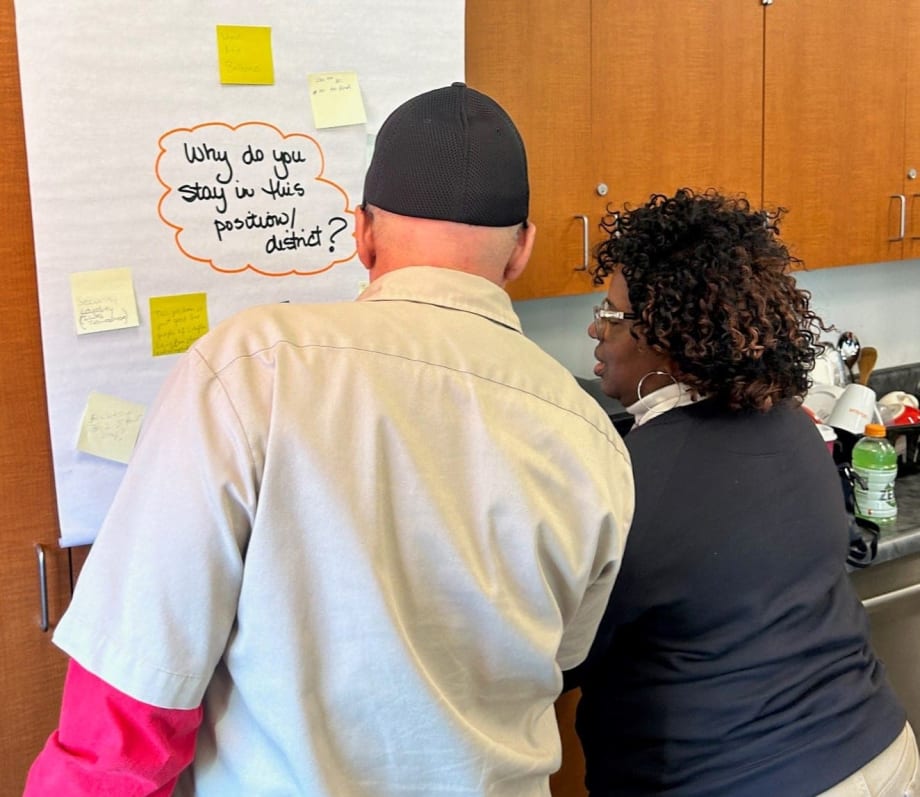 two people stand in front of a poster that says "why do you stay in this position?"