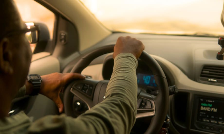 From the interior of a car, a man in a green long sleeve shirt is driving.