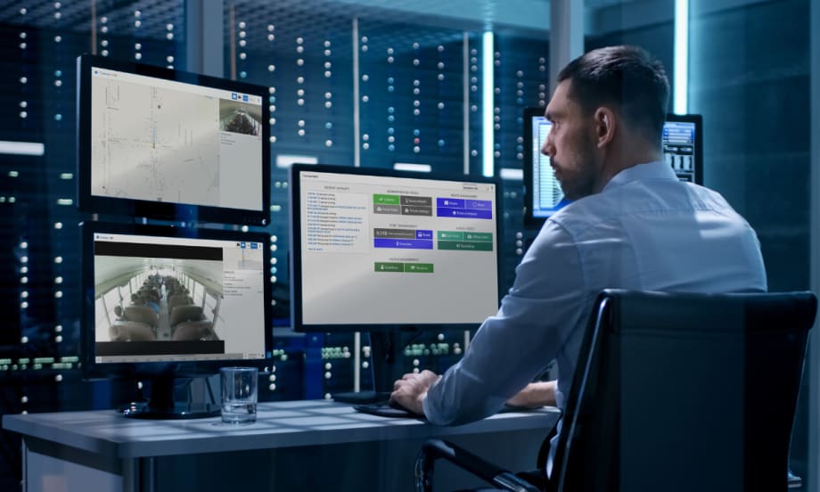 A man sits at a desk with three computer monitors displaying Transportant's platform.