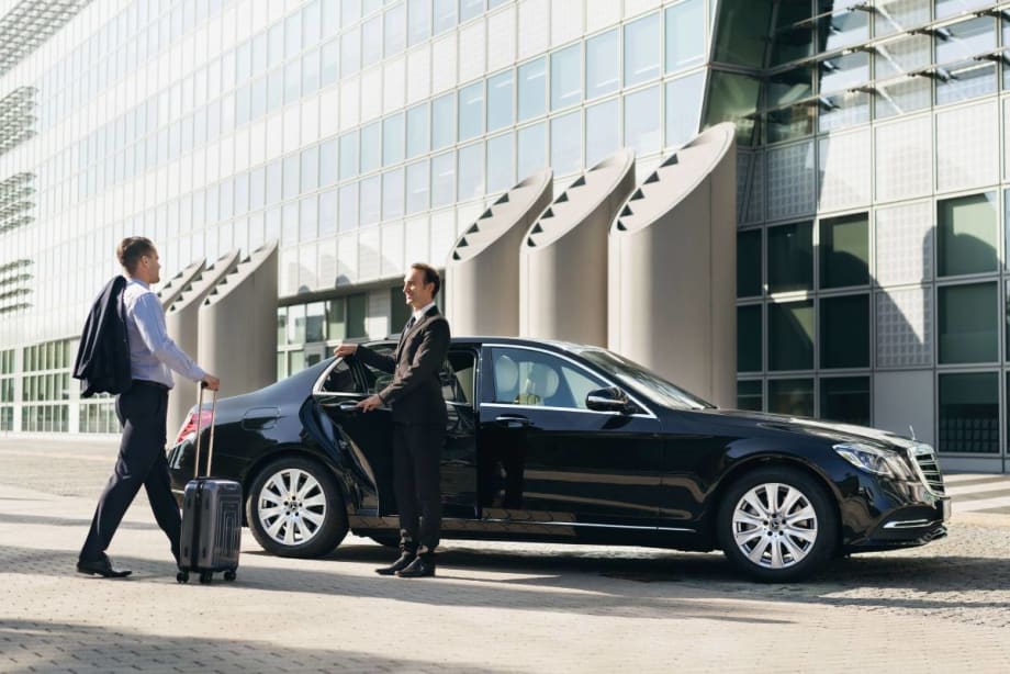 Chauffeured client being greeted by chauffeur steps into the back of a luxury black Mercedes-Benz operated by Blacklane.