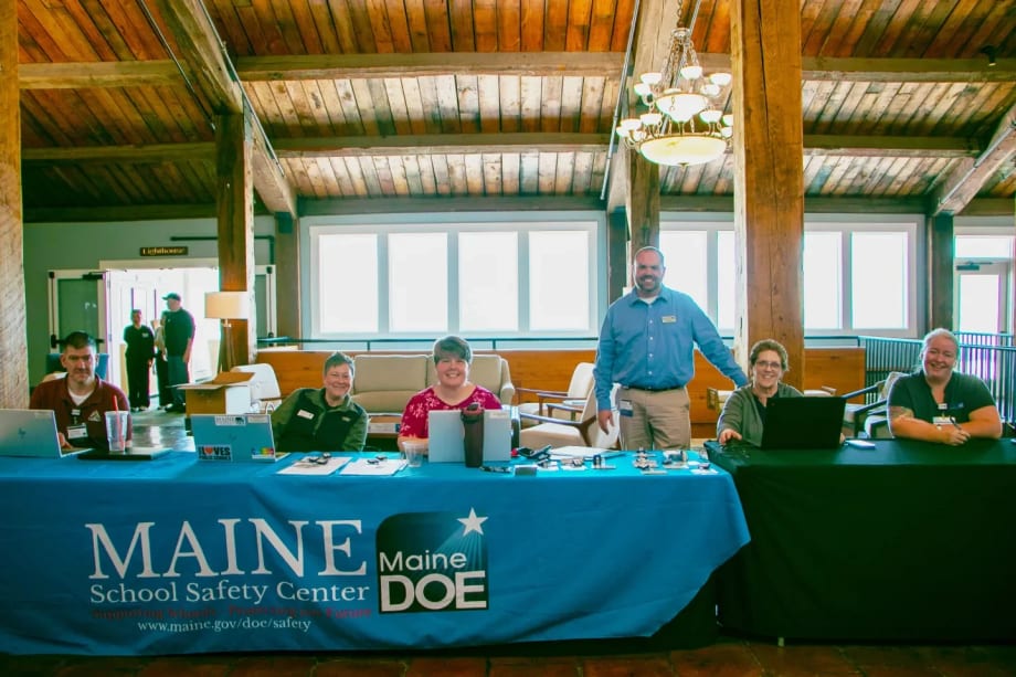 Conference registration table staffed by Maine School Safety Center team members assisting attendees with check-in at a school safety and transportation event.