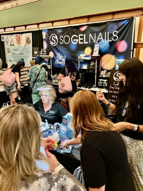 SO Gel Nails booth with owner Becky Bunnell standing on the right, engaging with attendees.