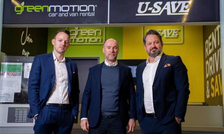 Three U-Save executives in suits pose in front of a rental car counter.
