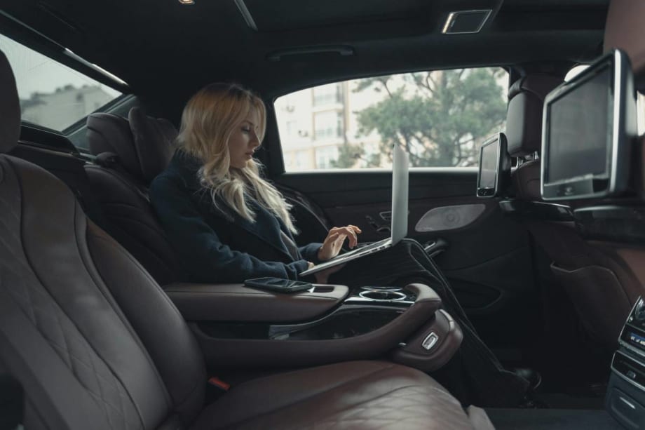 Businesswoman working on a laptop while riding in the backseat of a chauffeured car.