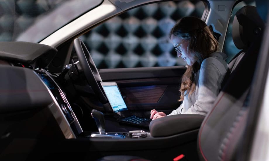 Data analyst looking at computer screen while seated in front of vehicle.