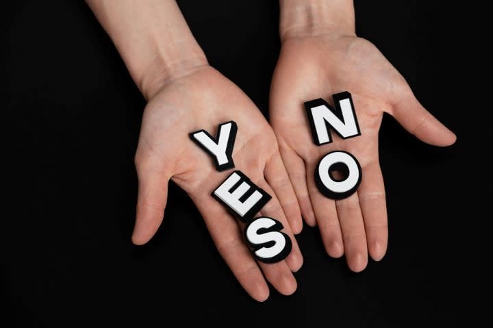 Two hands holding tiles that spell YES and No on a black background