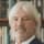 a man in a blue suit stands in front of a bookcase