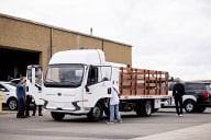 A lot of several vehicles, with the central vehicle being a medium-duty work truck with several workers inspecting it.
